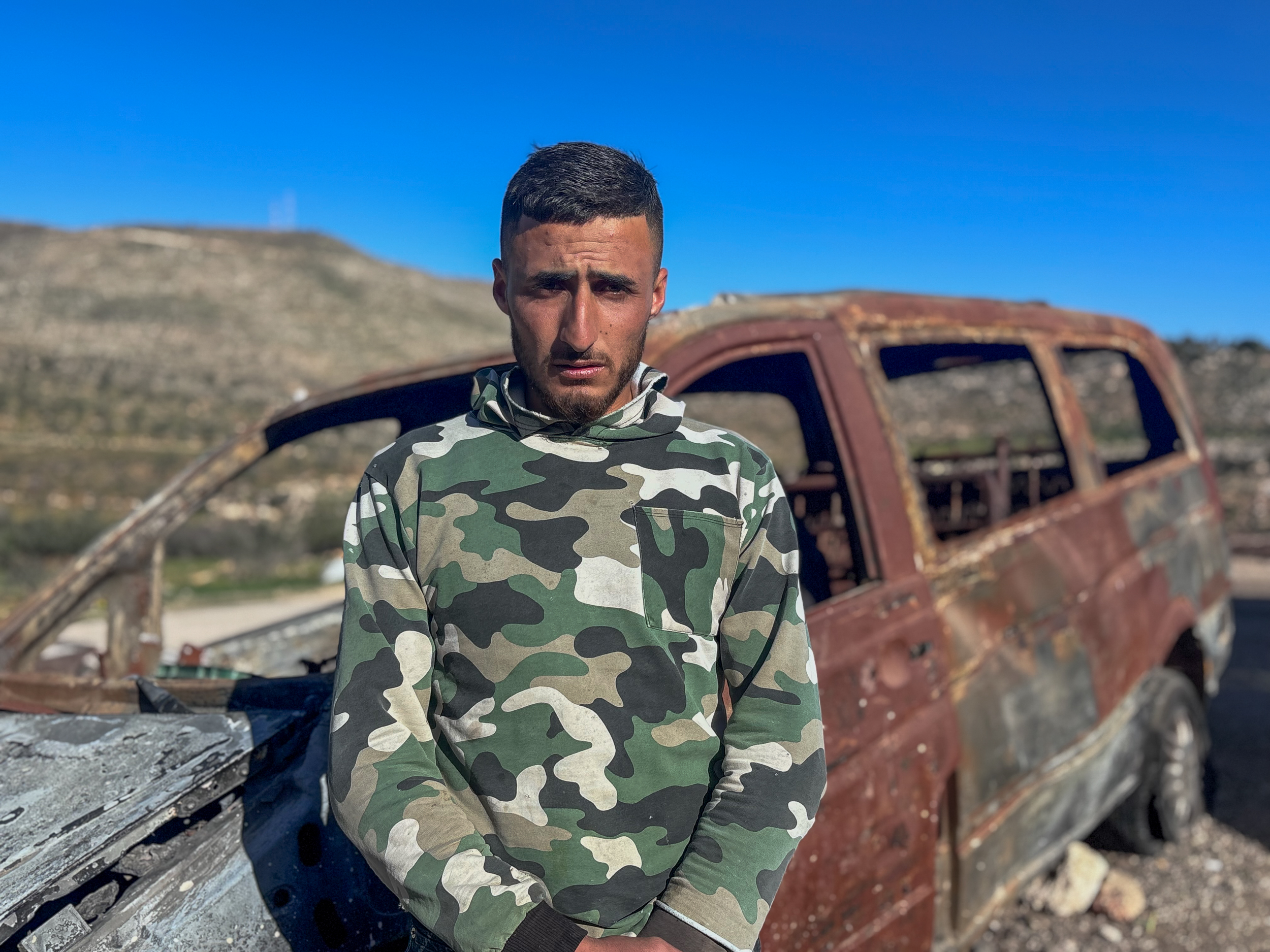 Thabet Masallam in front of the family car, torched by illegal Israeli settlers [Al Jazeera]