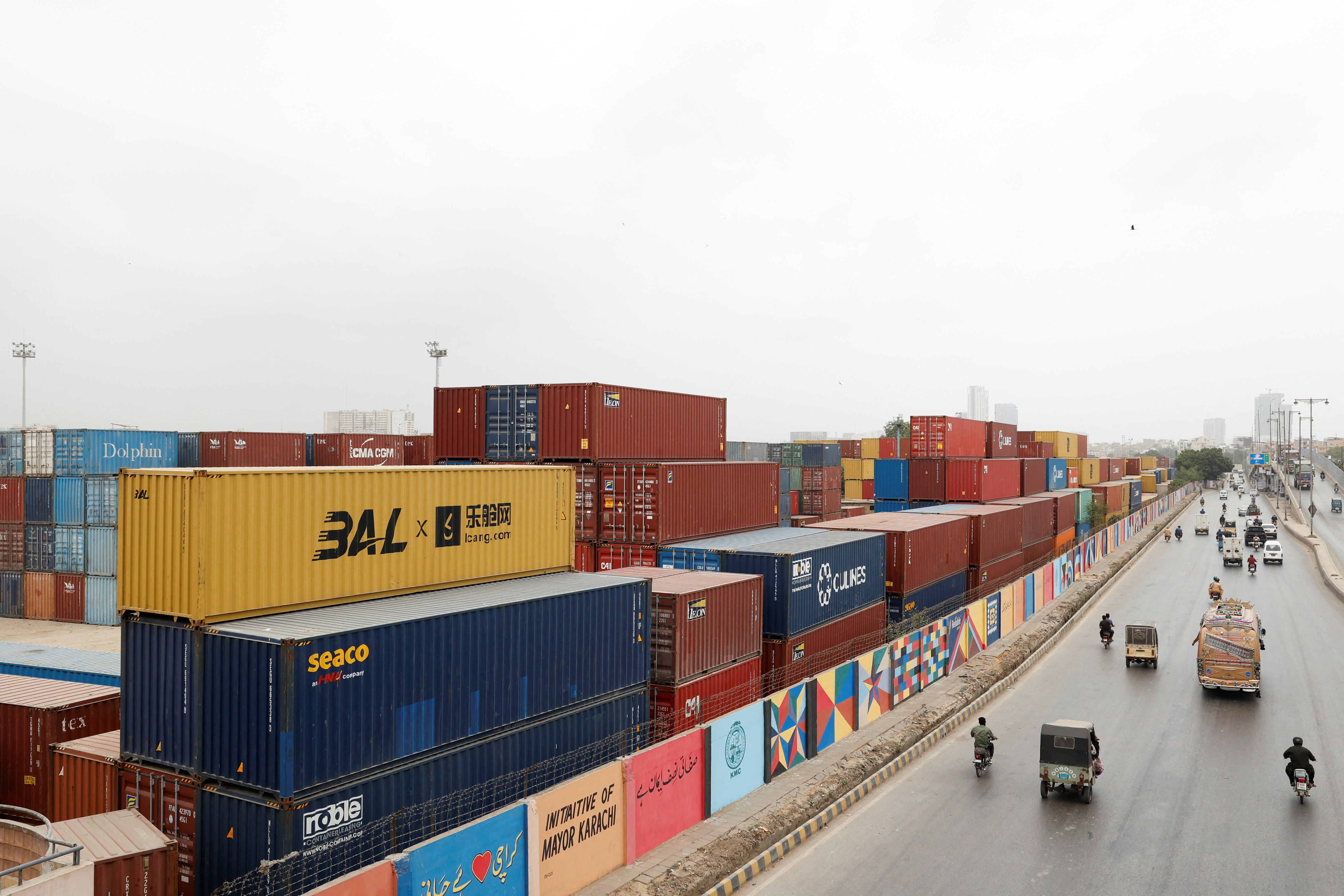 Vehicles move past a warehouse yard with shipping containers.