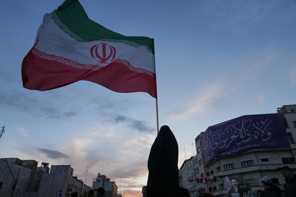 Roman in black stands by giant iranian flag