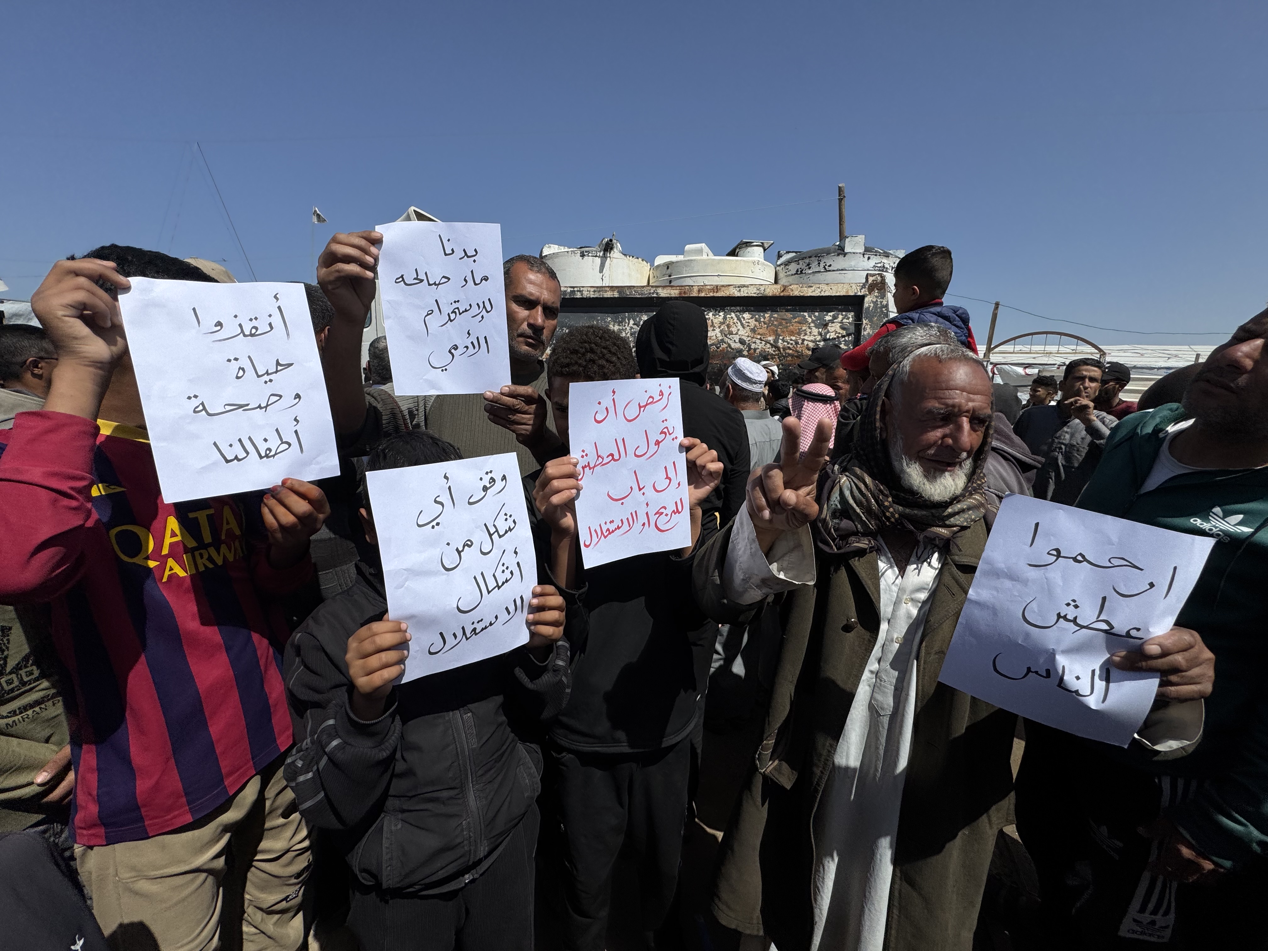 Protesters on Saturday in al-Mawasi hold up small posters denouncing the lack of water [