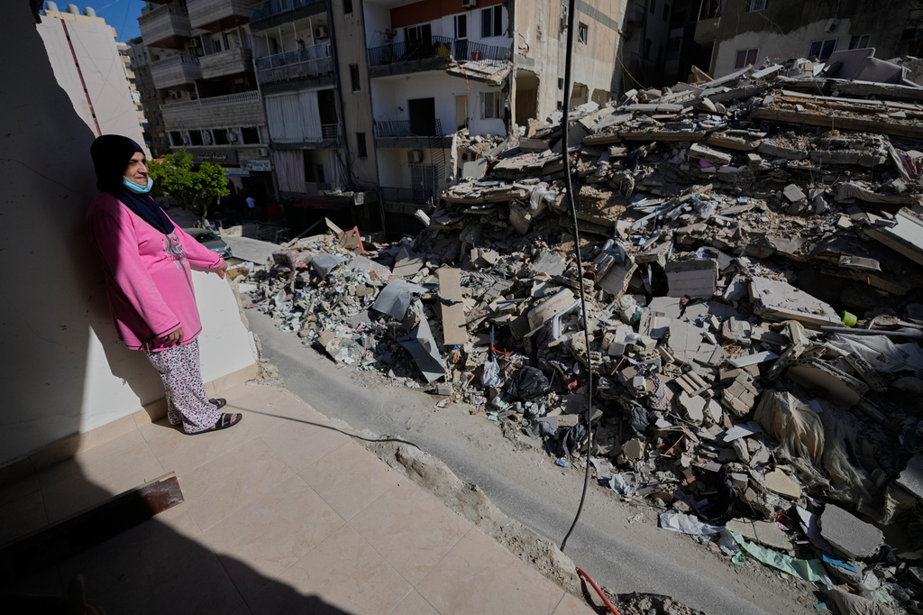 Woman stands by ruins of a house