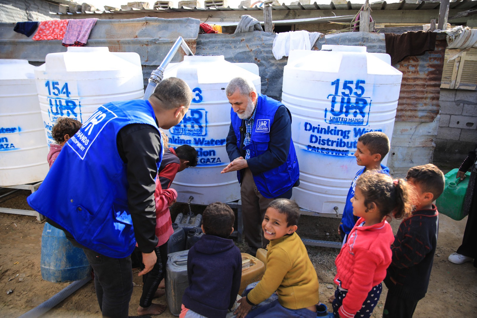 UHR CEO, Suleiman Alghanem, and child beneficiaries refill water containers from a UHR-sponsored water tank