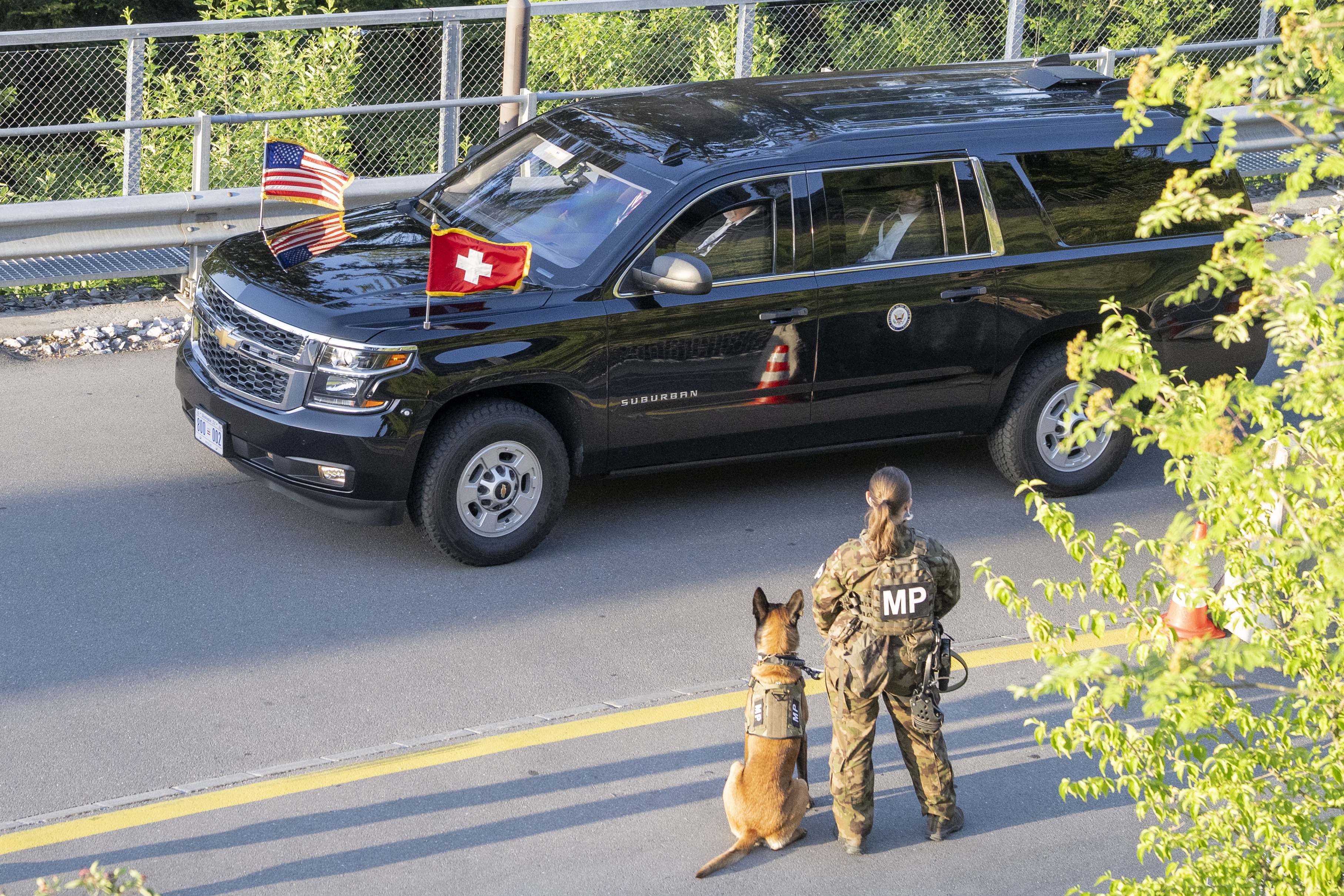 A soldier with a dog in front of an armoured car with the US and Swiss flags on it.