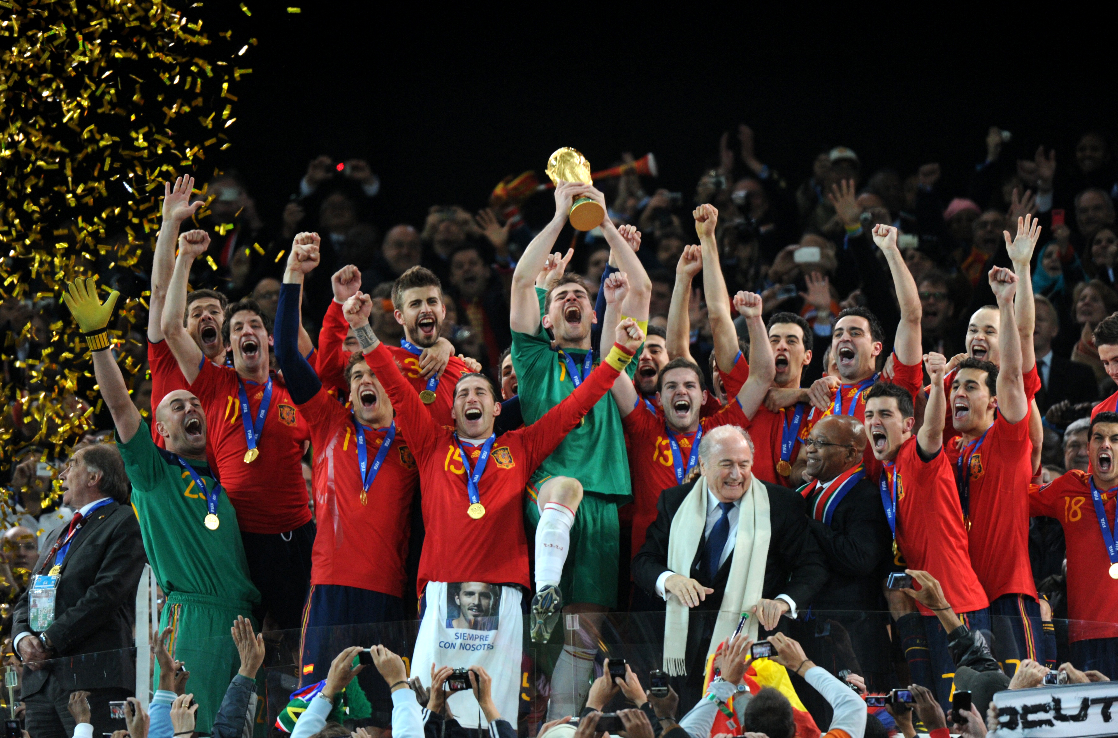 Spain's goalkeeper Iker Casillas (C) raises the trophy as Spain's national football team players celebrate with FIFA President Sepp Blatter (5thR) and South Africas President Jacob Zuma (4thR) winning the 2010 World Cup football final Netherlands vs. Spain on July 11, 2010 at Soccer City stadium in Soweto, suburban Johannesburg. NO PUSH TO MOBILE / MOBILE USE SOLELY WITHIN EDITORIAL ARTICLE - AFP PHOTO / GABRIEL BOUYS (Photo by GABRIEL BOUYS / AFP)