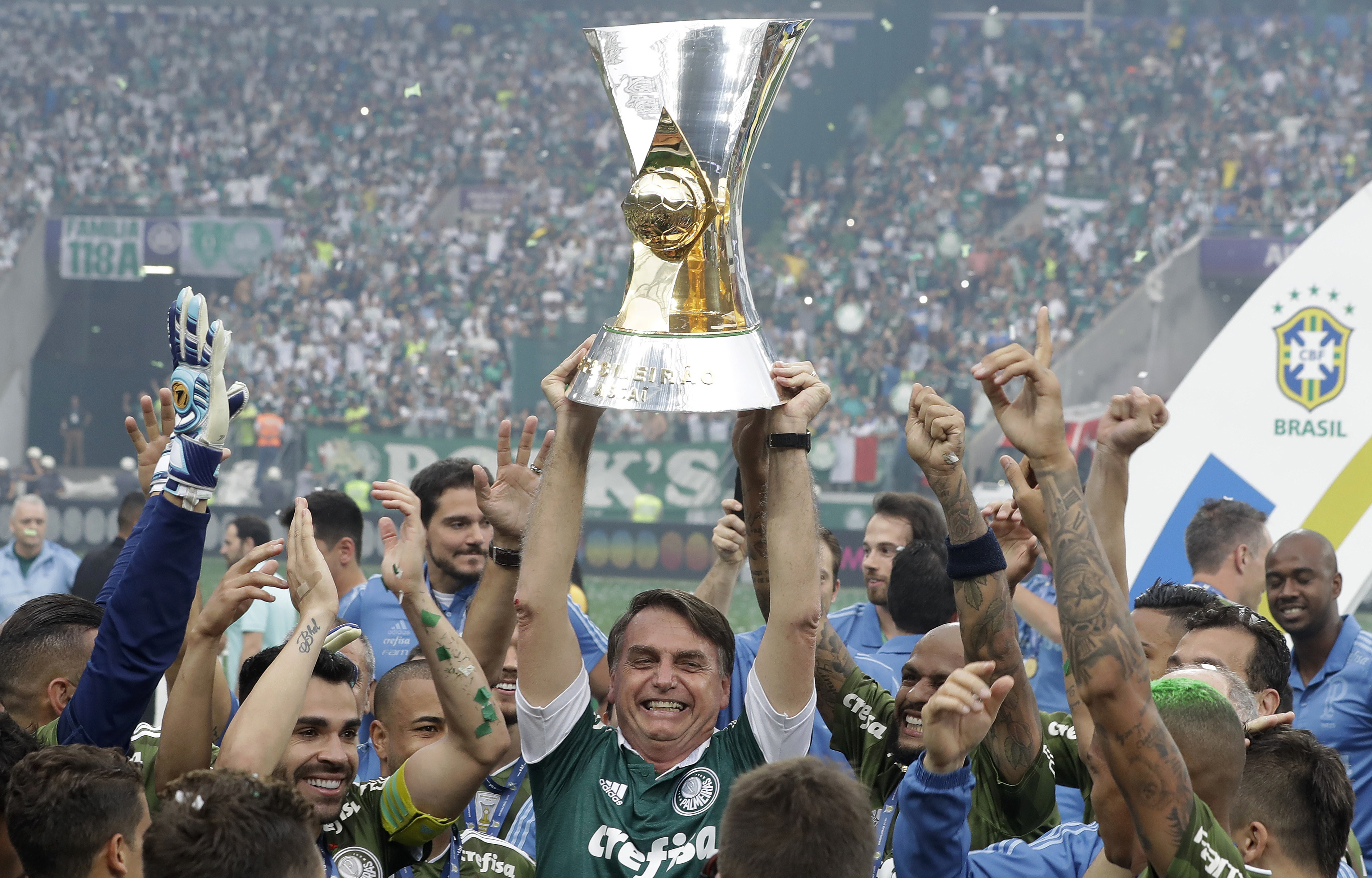Brazil's President-elect Jair Bolsonaro holds up the Brazilian soccer championship trophy, as he celebrates with Palmeiras soccer club who won the title after defeating Vitoria, in Sao Paulo, Brazil, Sunday, Dec. 2, 2018. (AP Photo/Andre Penner)