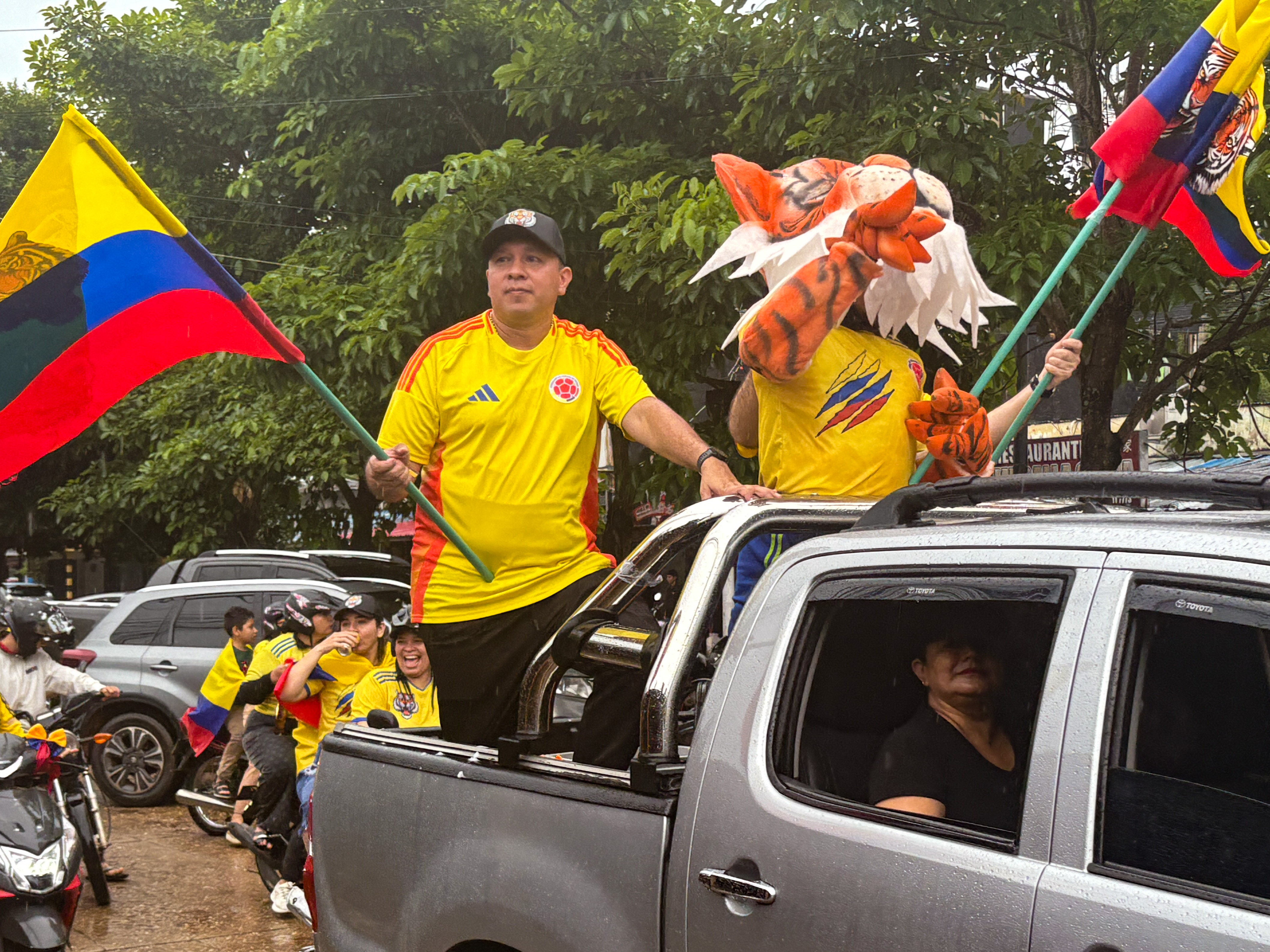 A man in a football jersey rides in the back of a truck with a tiger mascot