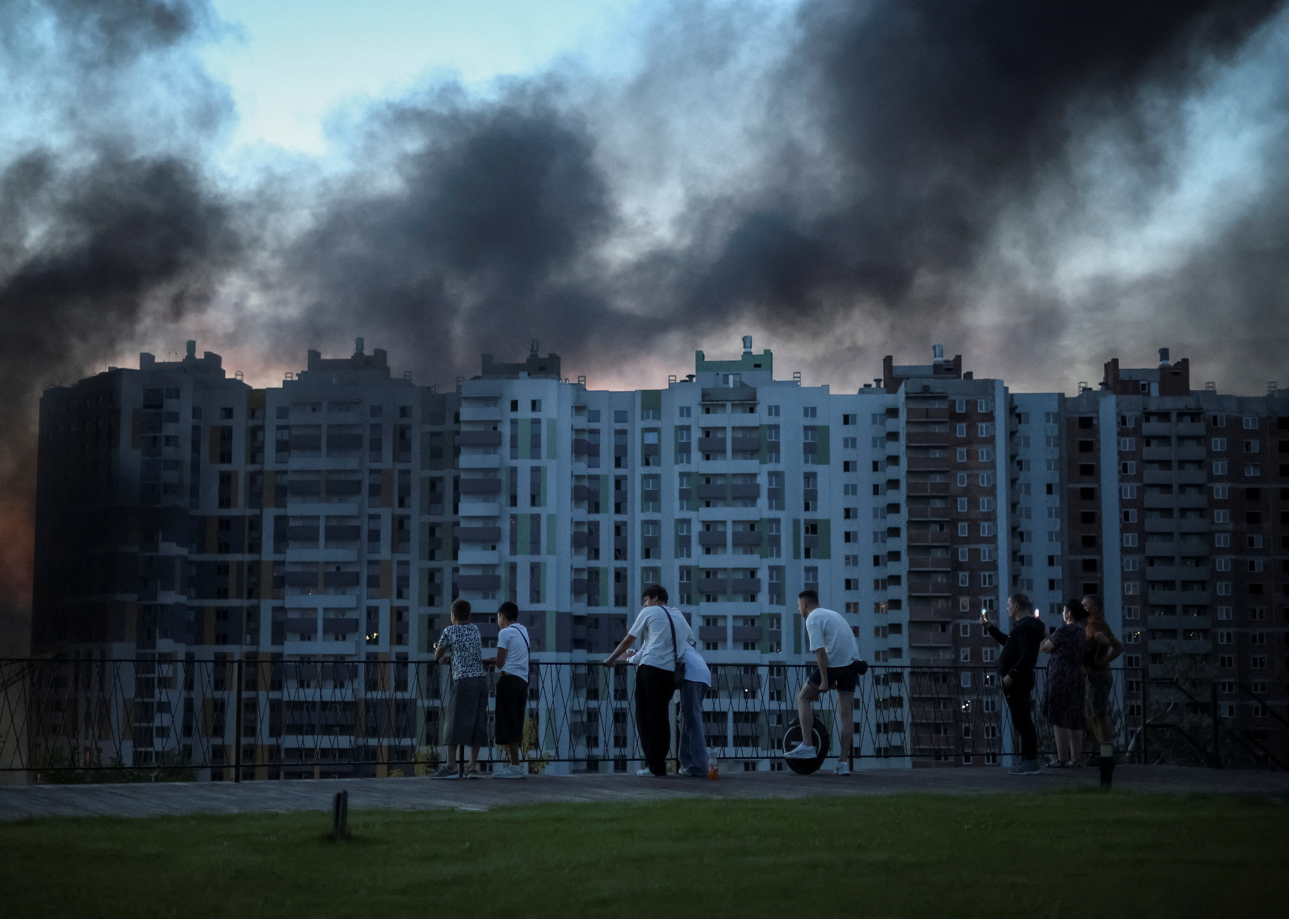 People look at smoke rising above buildings.