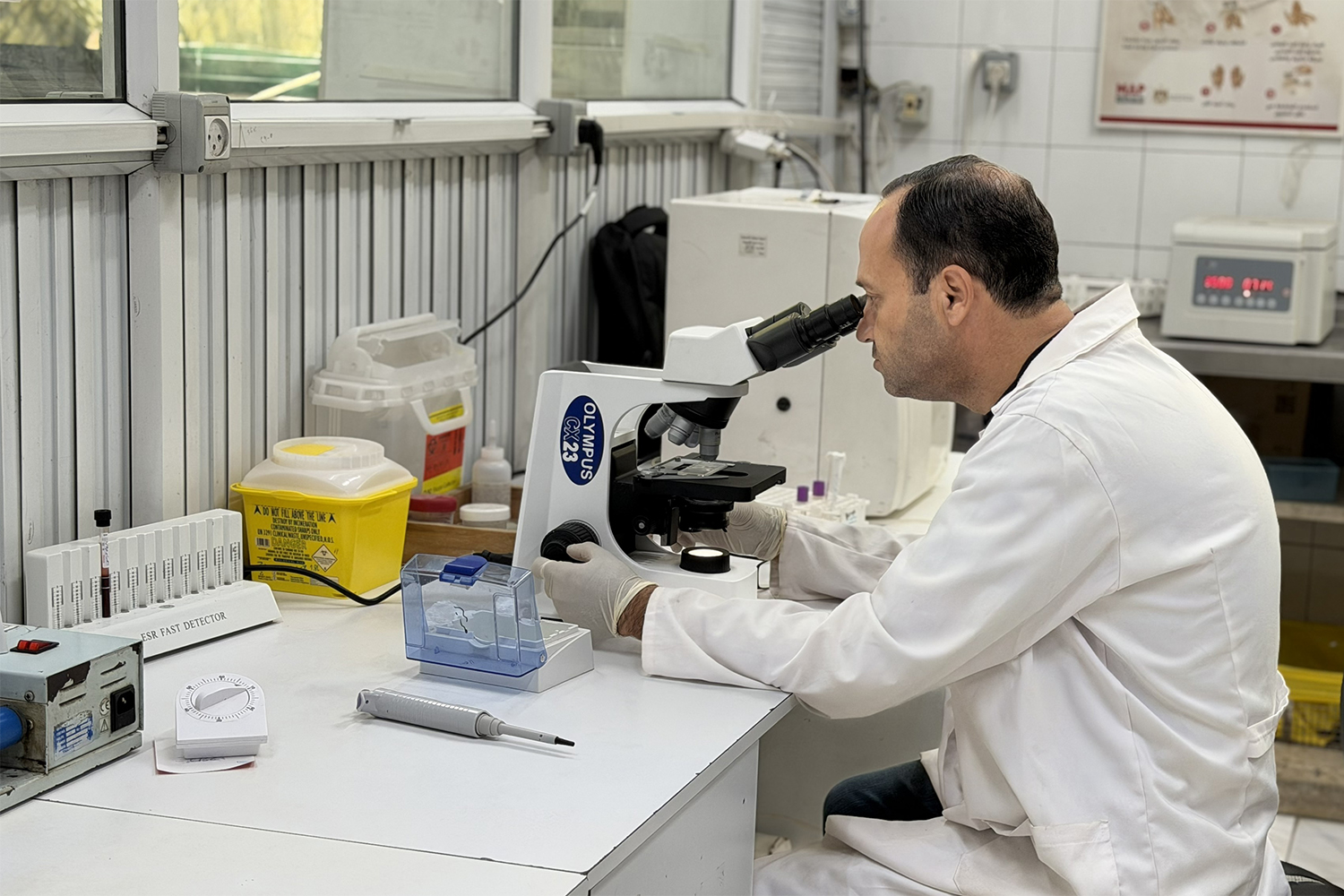 A laboratory technician performs a microscopic laboratory examination amid shortages and limited availability of medical supplies