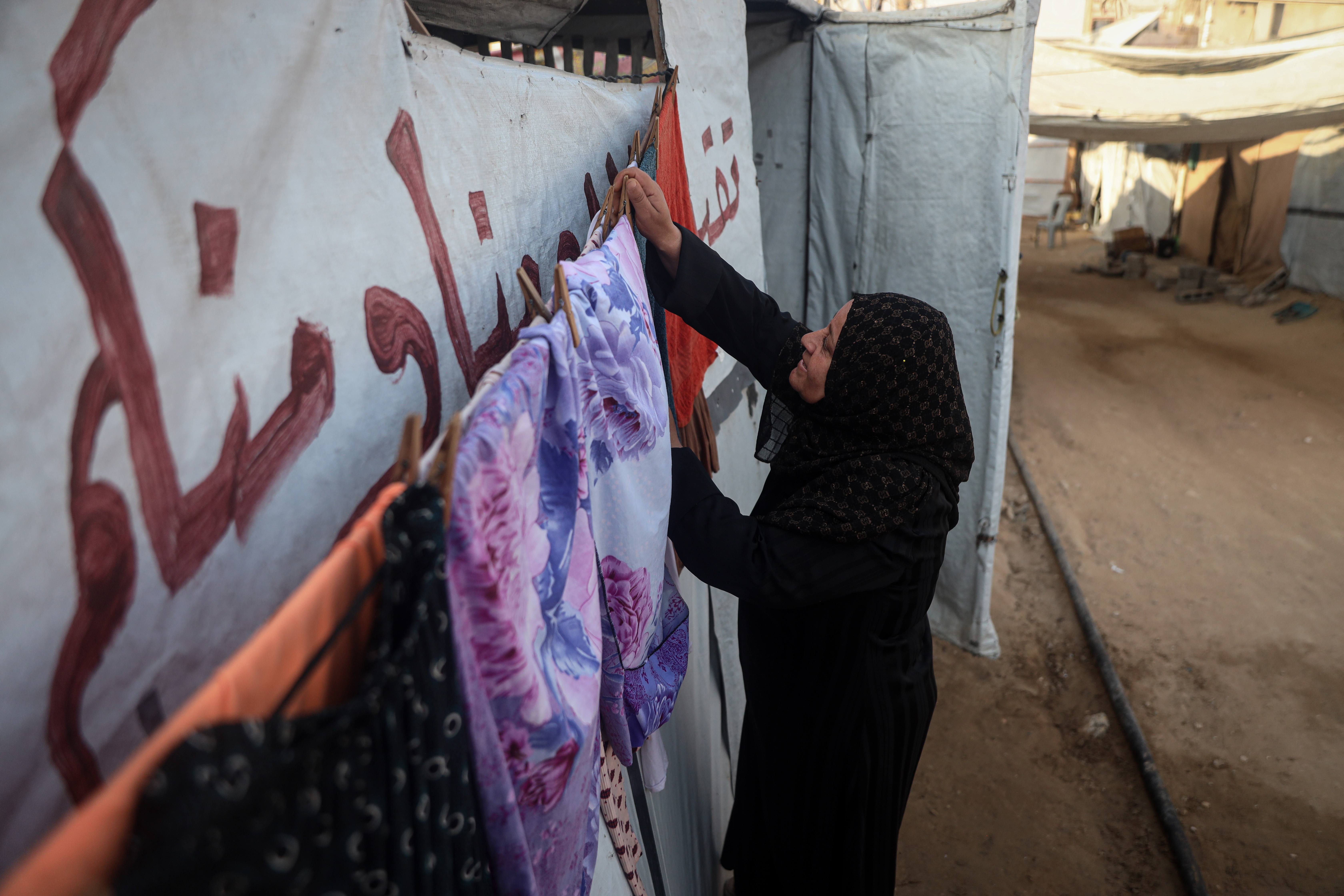 Abeer Ghorab, 52, a displaced Palestinian woman, takes her clothes to a commercial laundry, paying to wash and dry them as water and electricity remain scarce. [Abdelhakim Abu Riash/ Al Jazeera]