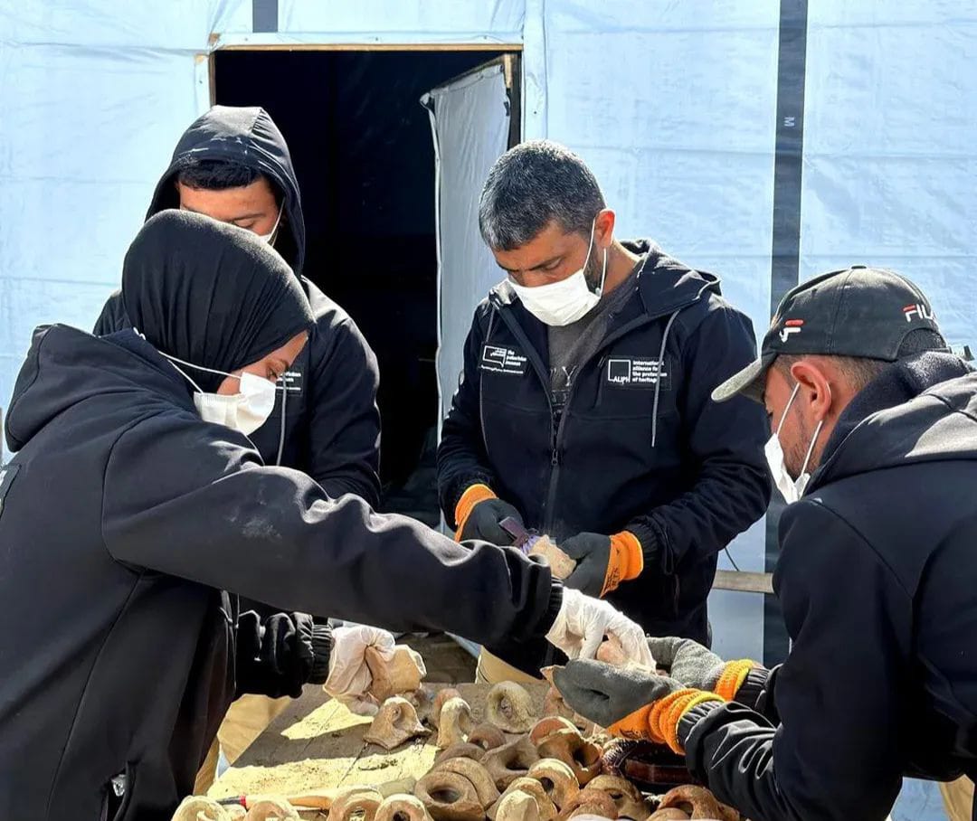 Members of the Guardians of Heritage team inspect and clean recovered archaeological pottery inside a temporary storage tent in al-Mawasi, the southern Gaza Strip
