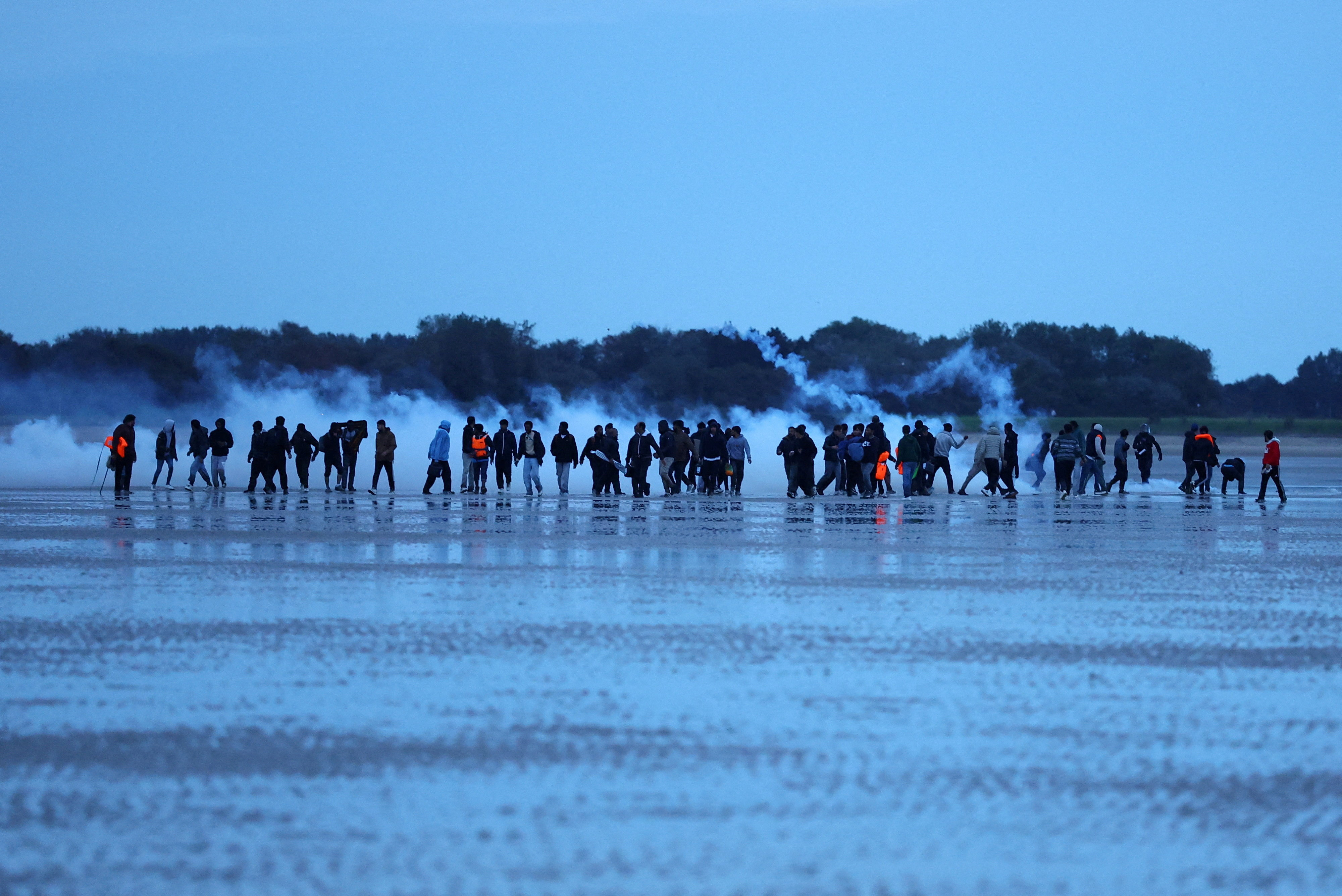 Migrants react to tear gas fired by police as they try to leave the coast of northern France in an attempt to cross the English Channel to reach Britain