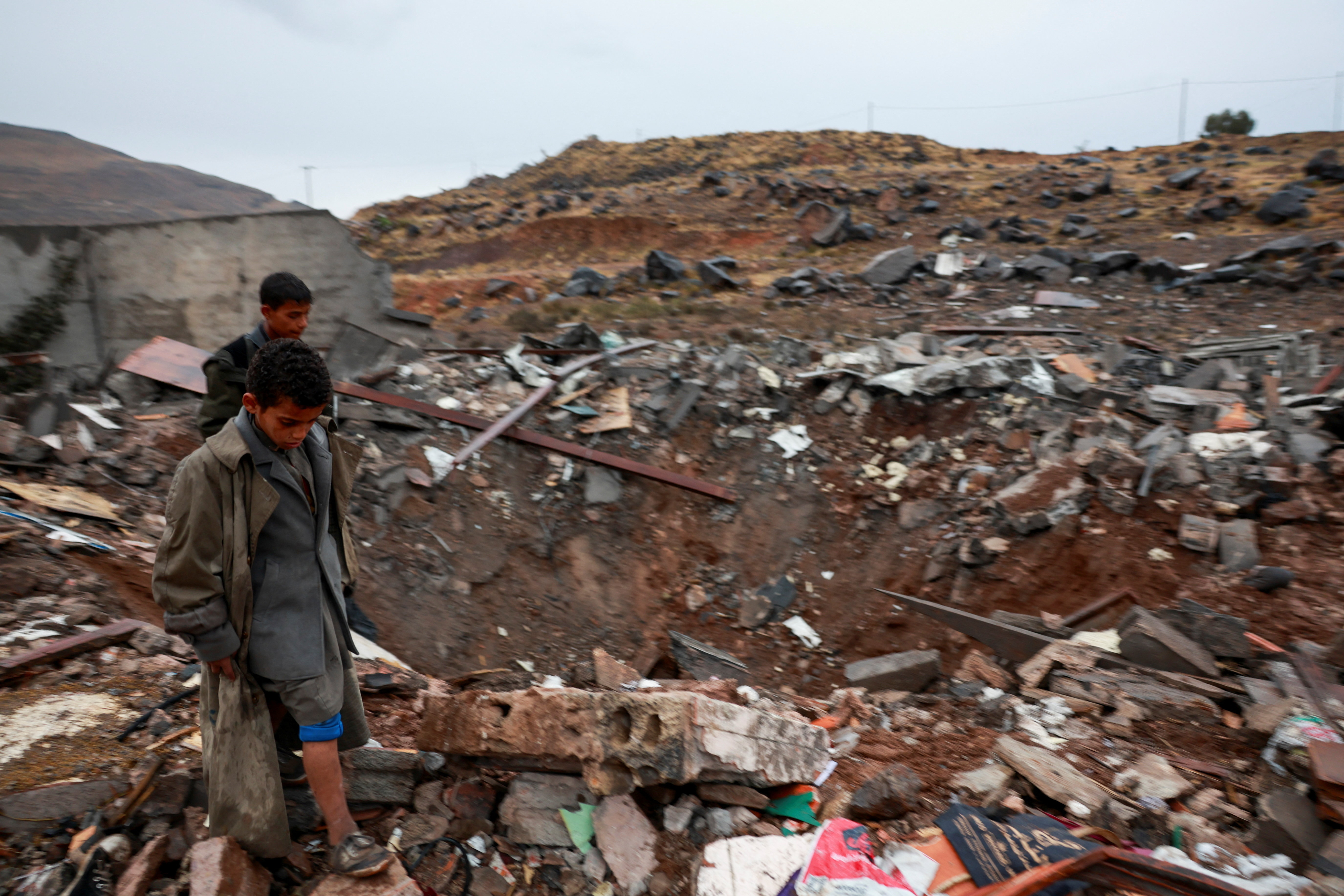 Boys walk next to a crater at the site of an airstrike on the outskirts of Sanaa, Yemen October 24, 2026. [Khaled Abdullah/Reuters]