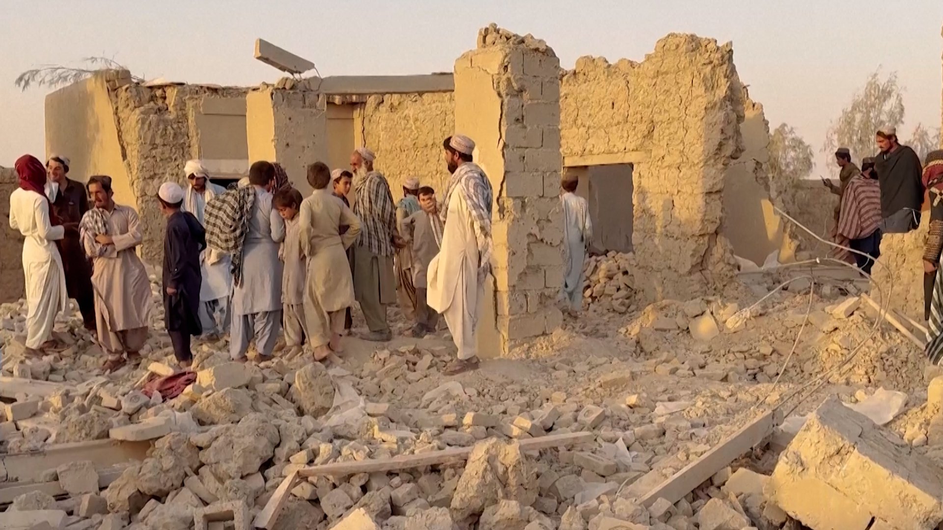 People standing by a destroyed home in Afghanistan